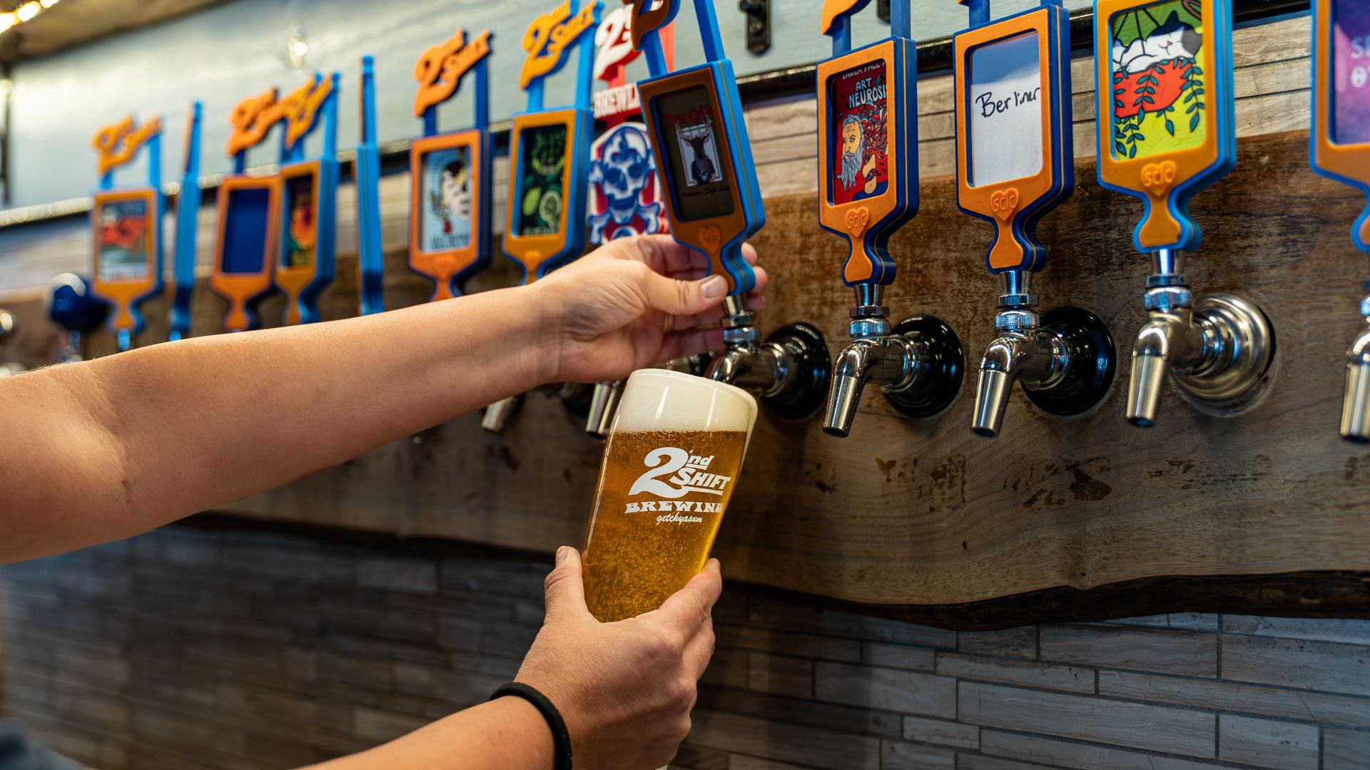 A bartender pours a beer from a colorful tap at 2nd Shift Brewing.