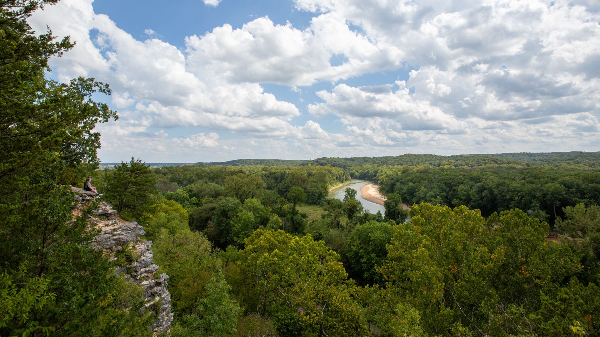 Hikers perch on a limestone bluff overlooking a river at Castlewood State Park.
