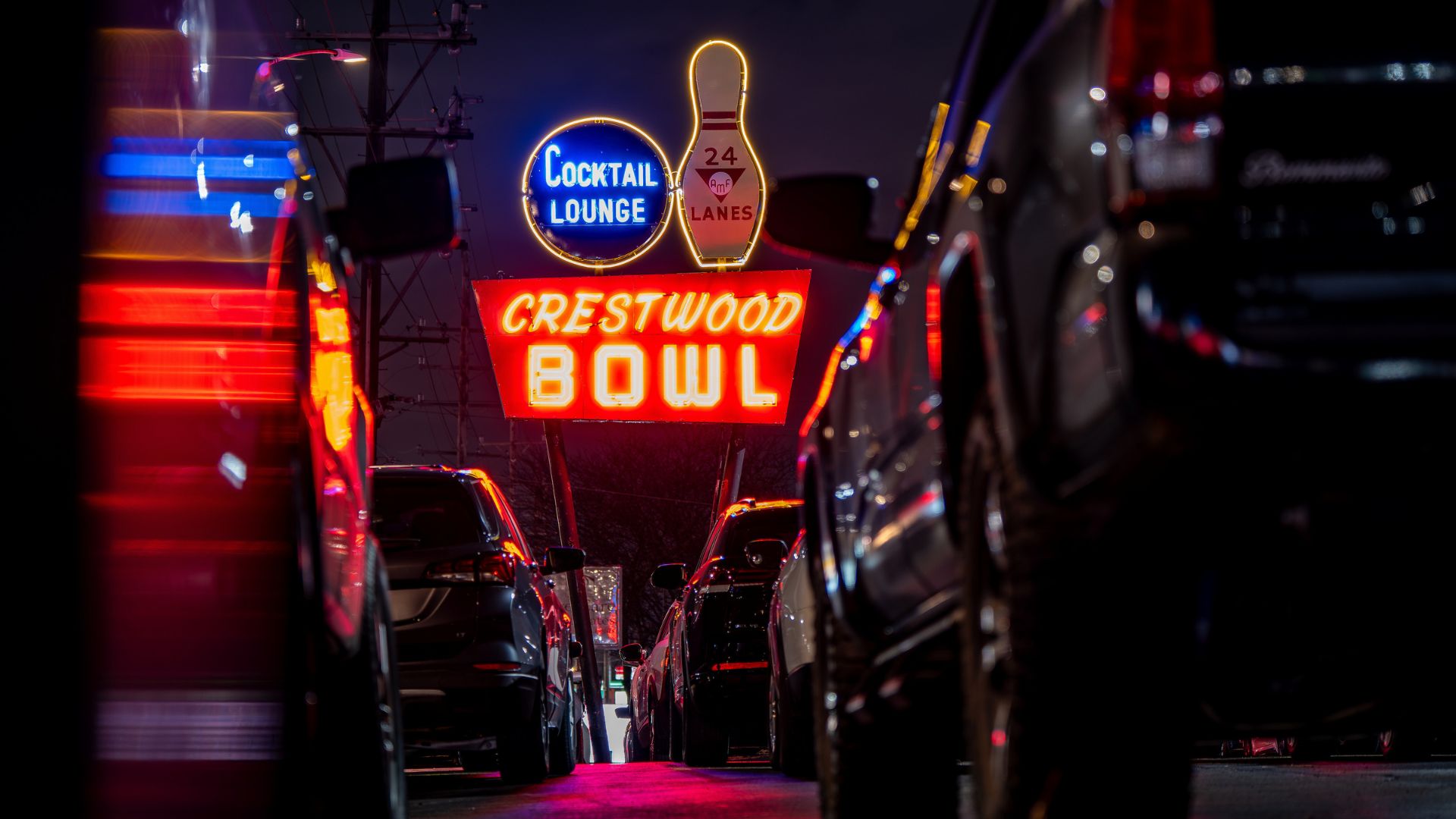 Through the cars in the parking lot, the Crestwood Bowl neon sign glows along Route 66.