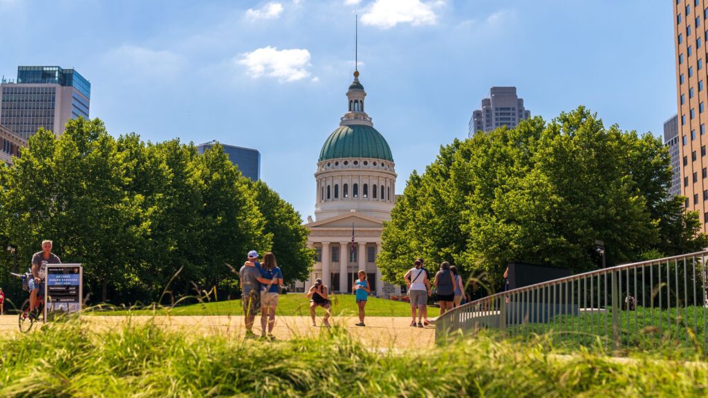 Visitors take photos in Gateway Arch National Park with the Old Courthouse in the background.