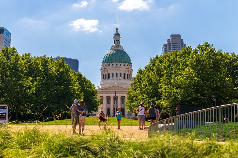 Visitors take photos in Gateway Arch National Park with the Old Courthouse in the background.