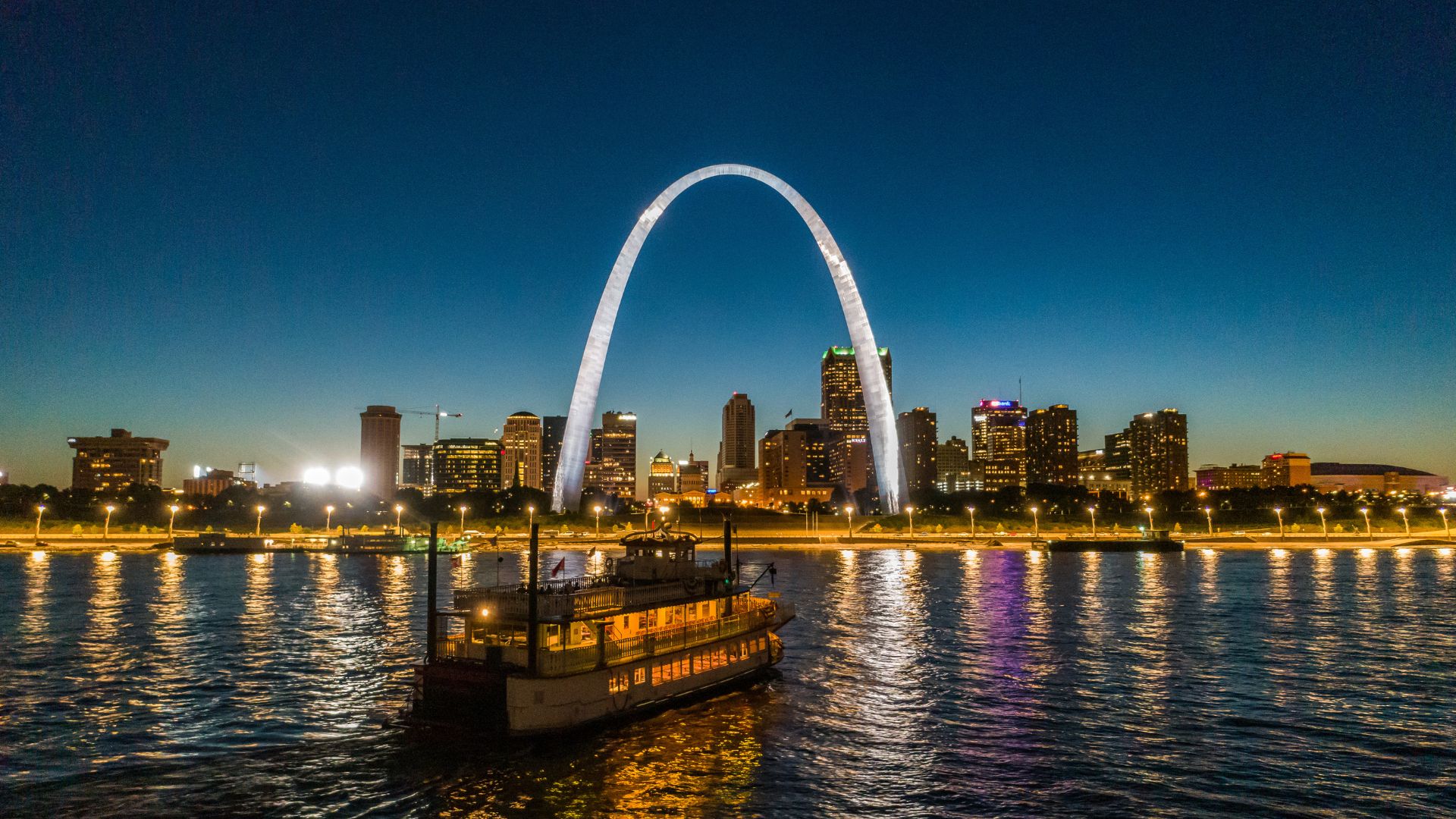 The Riverboats at the Gateway Arch glide along the Mississippi River at dusk.
